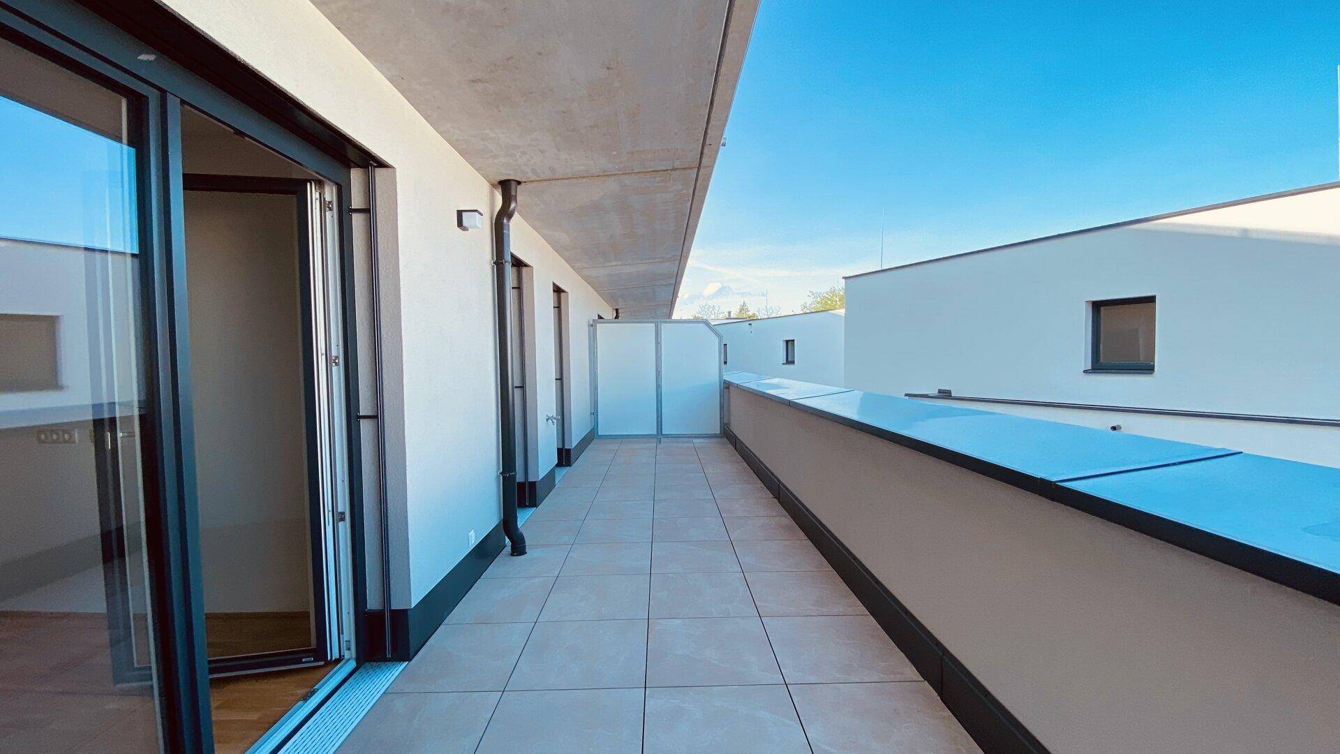 Geräumiger Balkon mit Fliesenboden und Blick auf die umliegenden Gebäude und den Himmel.