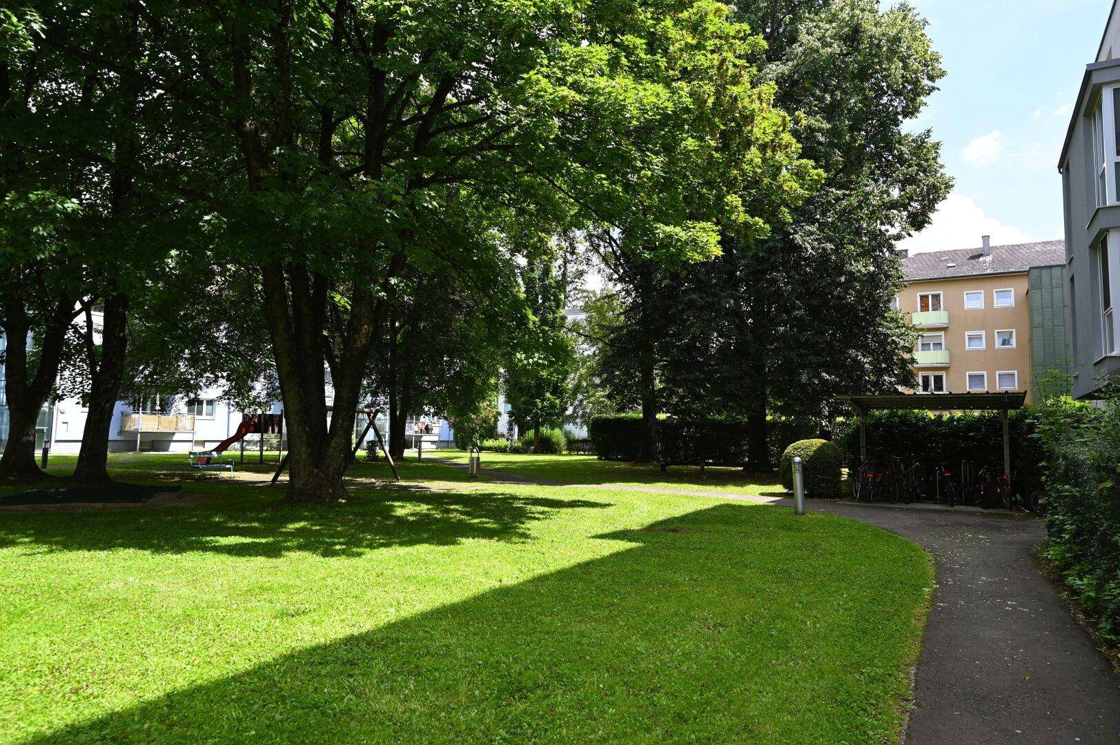 Großer Gemeinschaftsgarten mit Rasenflächen, Bäumen und einem Spielplatz für Kinder.