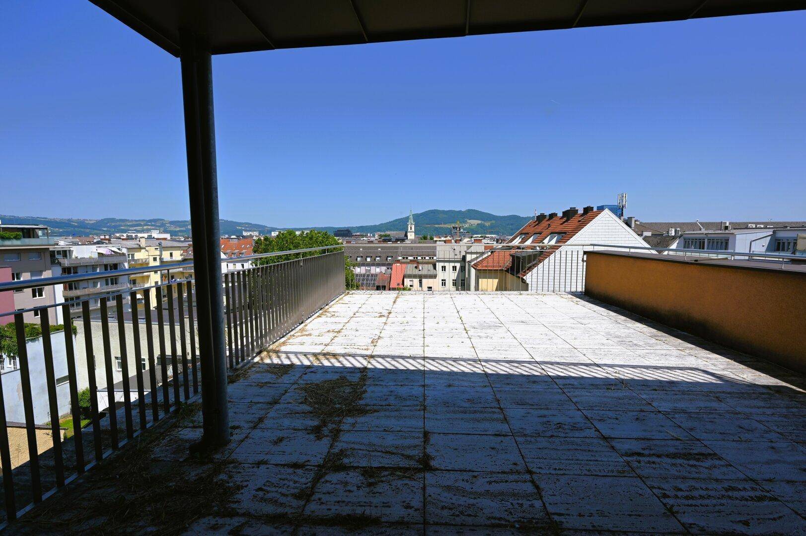 Große Außenterrasse mit Fliesenboden und Metallgeländer, bietet einen weiten Blick über die Stadtlandschaft.