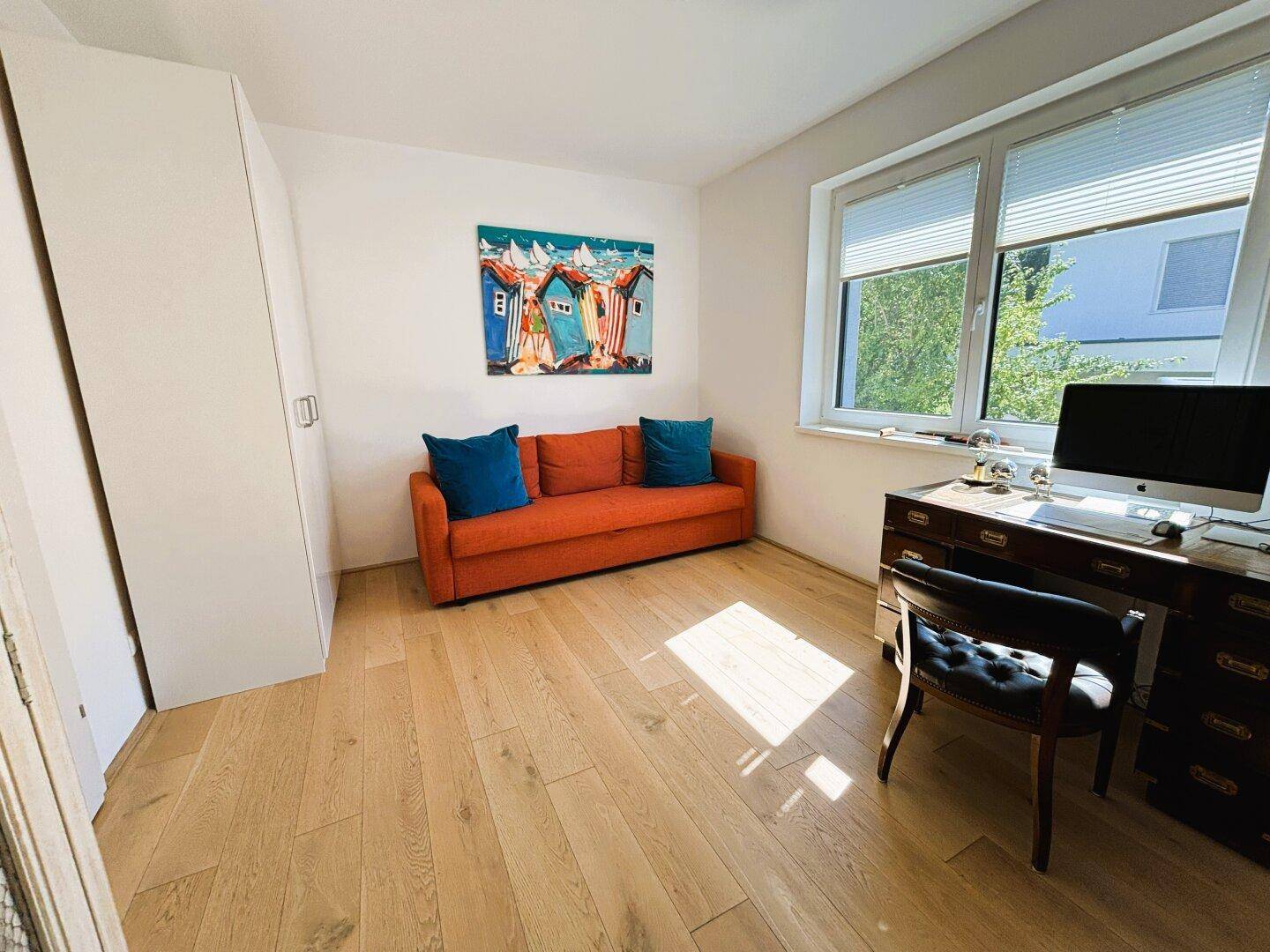 Gemütliches Zimmer mit Holzboden, Schreibtisch und Sofa.