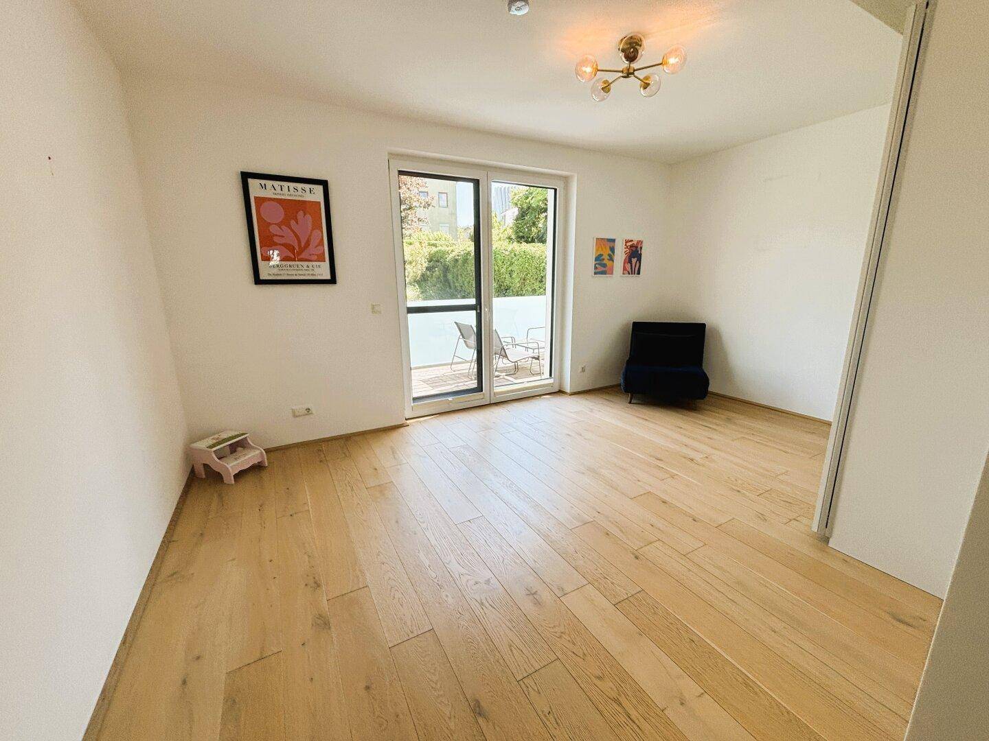 Helles Zimmer mit Holzboden und Zugang zu einem kleinen Außenbereich.