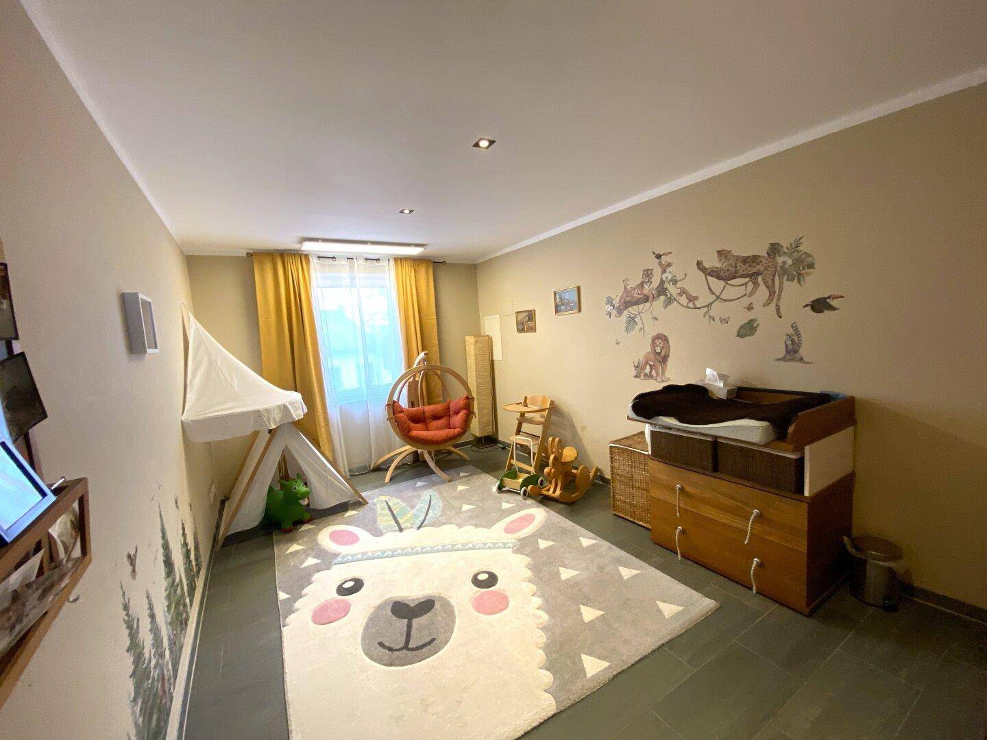Helles Kinderzimmer mit Wickelkommode, Spielzelt und farbenfrohem Teppich.