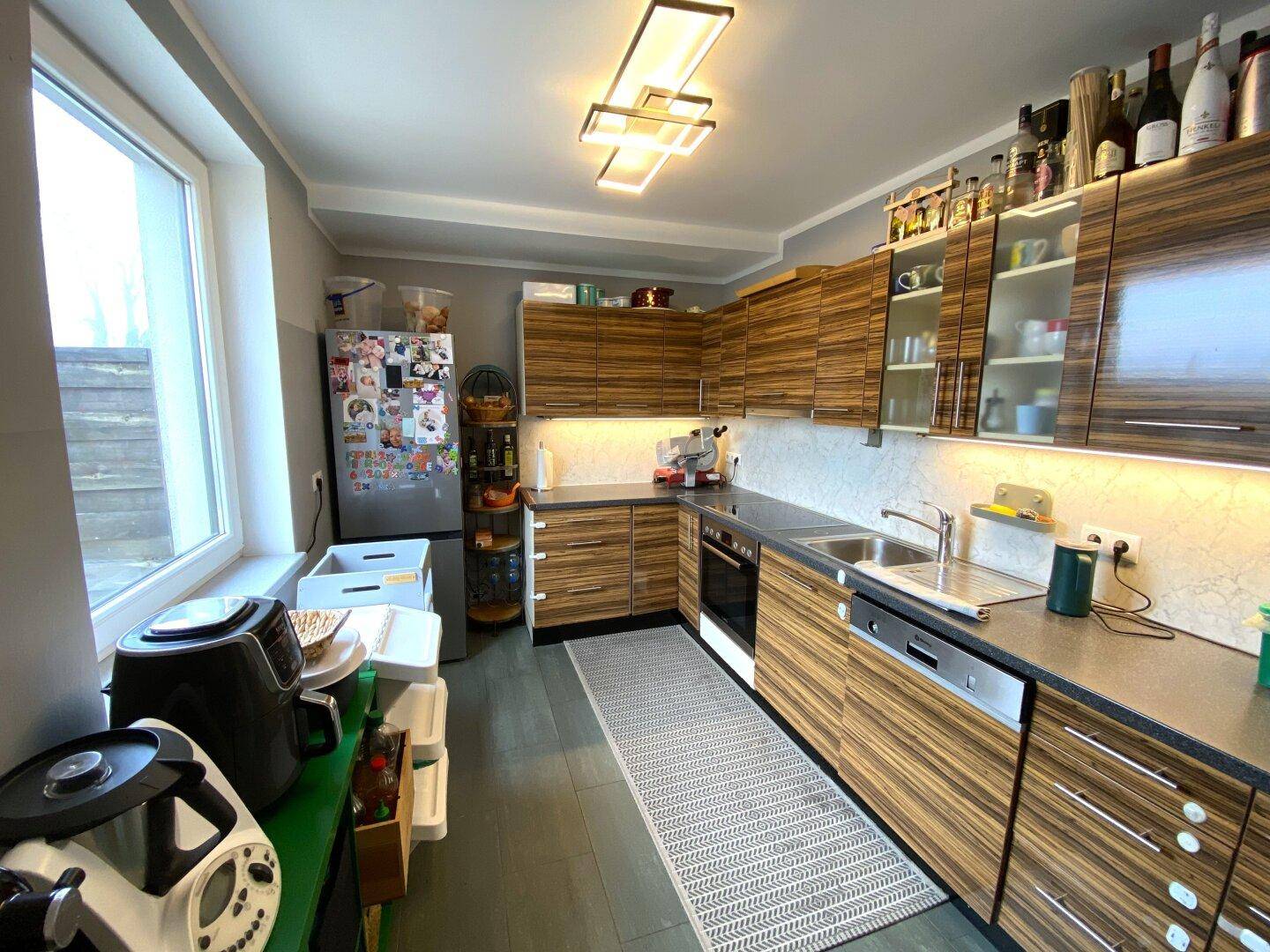 Moderne Küche mit Holzfronten, Einbaugeräten und großem Fenster für viel Licht.