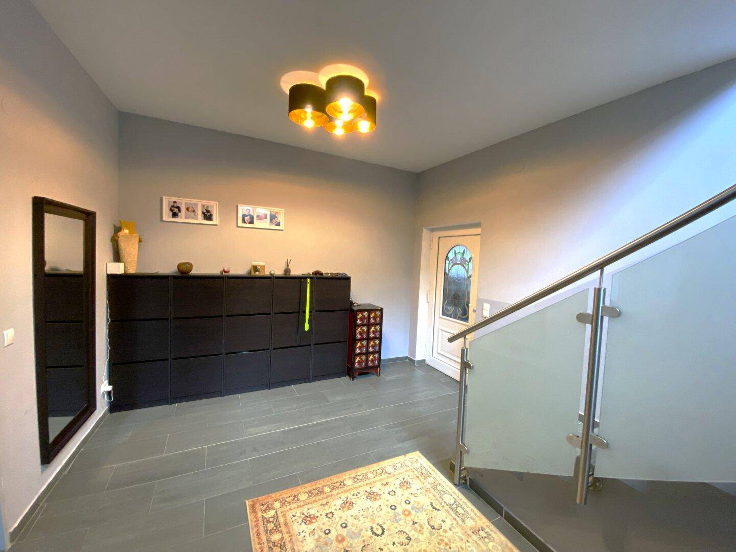Eingangsbereich mit Schuhschränken, Spiegel und Treppe mit modernem Glasgeländer.