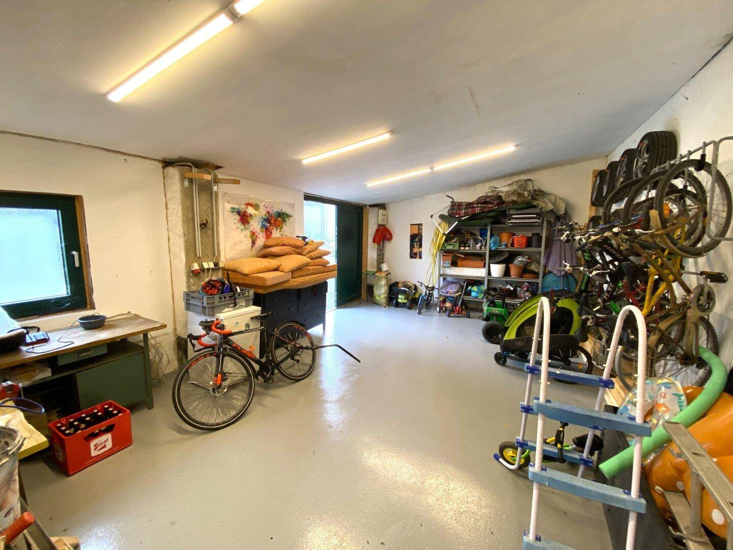 Geräumige Garage oder Abstellraum mit Fahrrädern, Werkzeugen und einem Fenster.