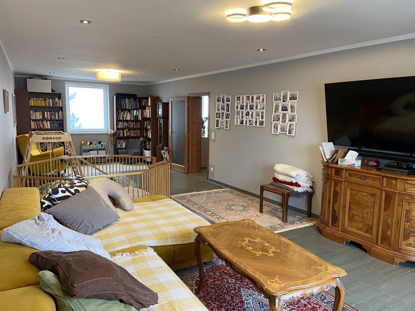 Helles Wohnzimmer mit großem Sofa, Teppich und Bücherregalen im Hintergrund.