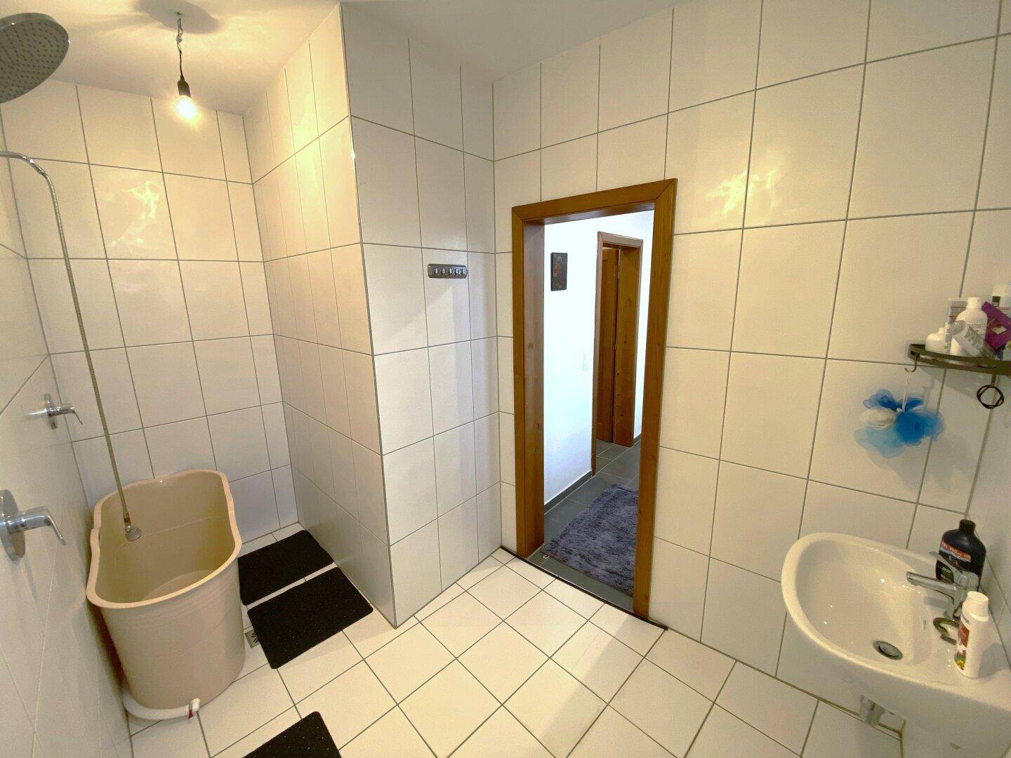 Badezimmer mit Duschbereich, Waschbecken und weißen Fliesen an Wänden und Boden.