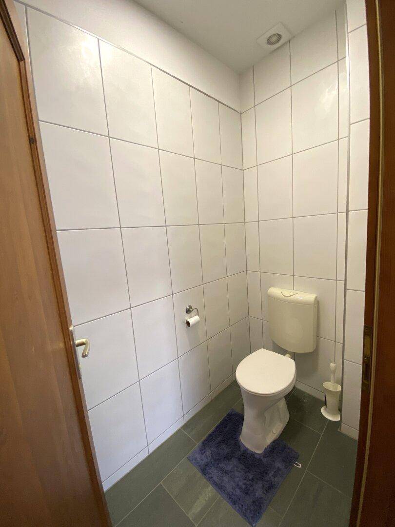 Einfaches WC mit Toilette und Fliesenboden, angrenzend an einen anderen Raum.