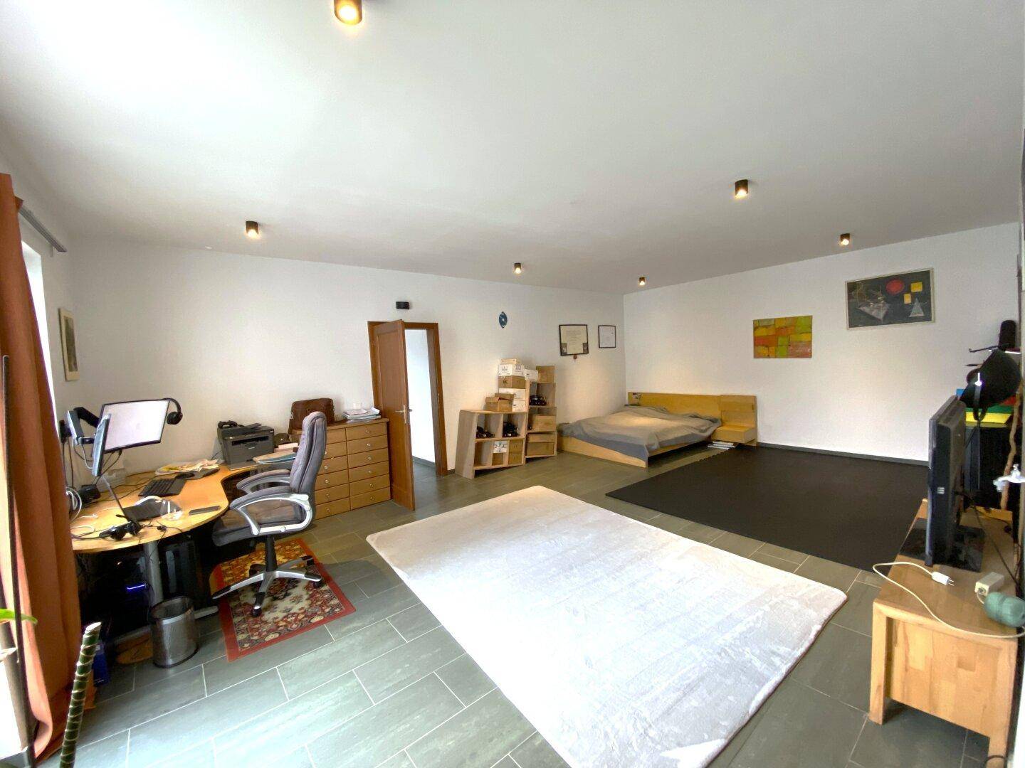 Großes Zimmer, eingerichtet als Büro und Schlafbereich, mit viel Tageslicht.