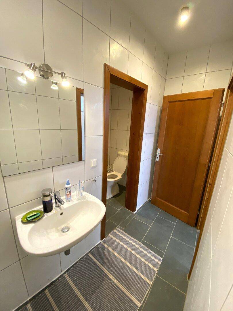 Badezimmer mit Waschbecken, Spiegel und Zugang zu einem separaten WC-Bereich.