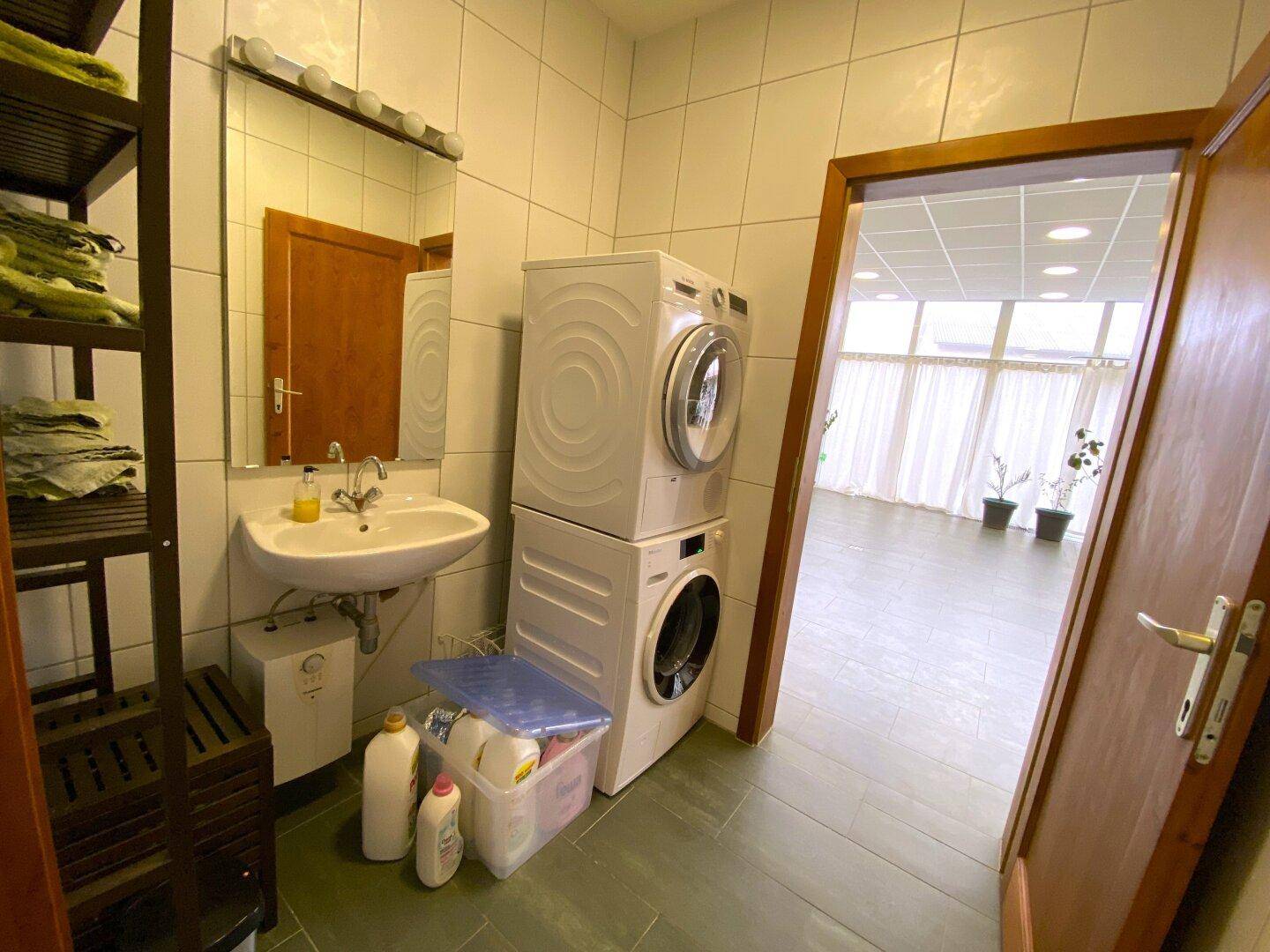 Hauswirtschaftsraum mit Waschmaschine, Trockner, Waschbecken und Regalen.