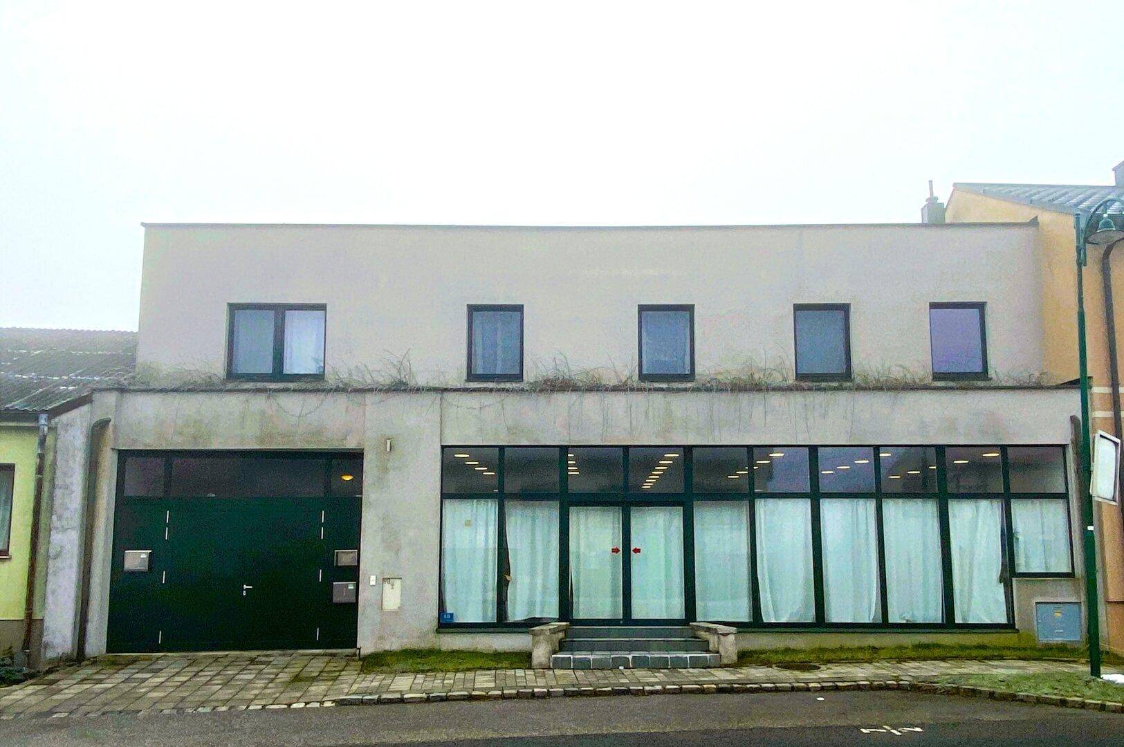 Moderne Gebäudefassade mit großen Fenstern und Garagentor an der Straßenseite.