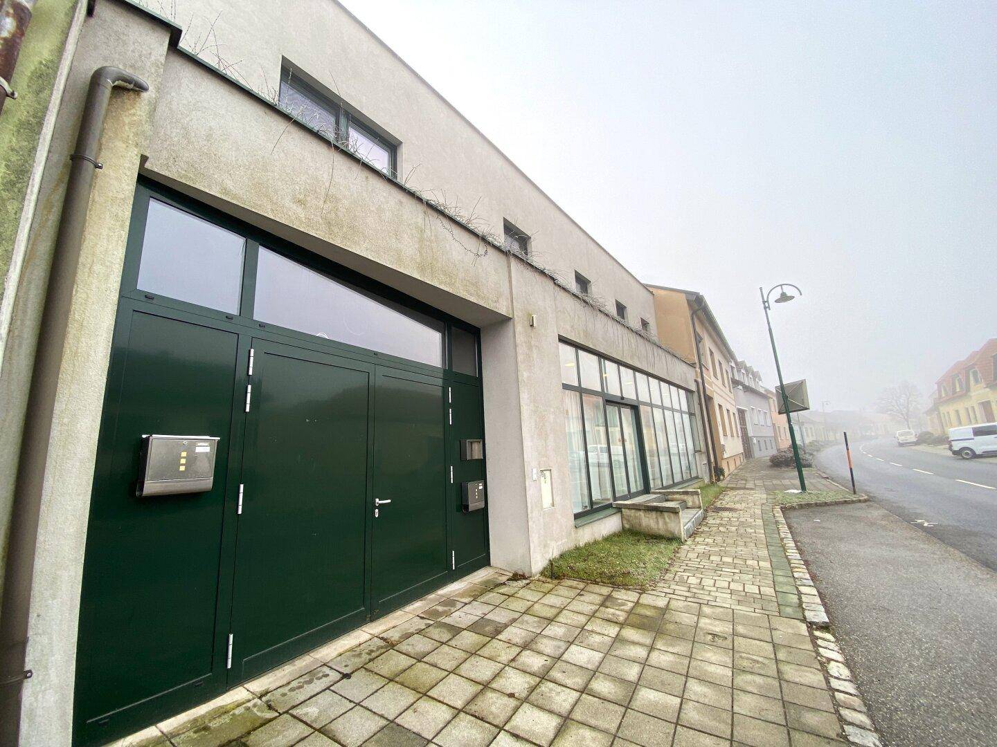 Gebäudefassade mit Garagentor und großen Fenstern an einer ruhigen Straße.