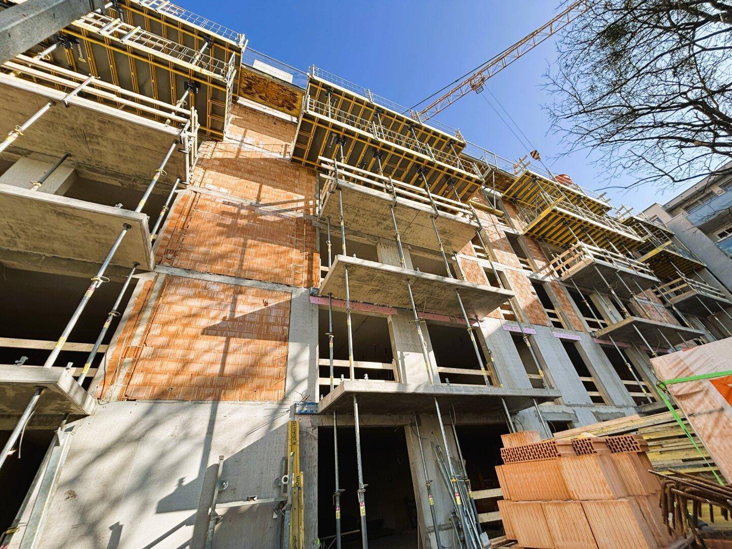 Fassade eines im Bau befindlichen Gebäudes mit mehreren Stockwerken, Gerüsten und Ziegelmauerwerk.