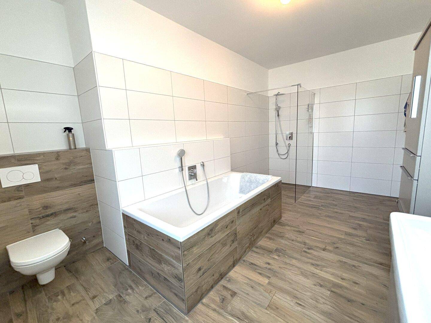 Modernes Badezimmer mit Badewanne, Dusche und Holzoptik-Fliesen.