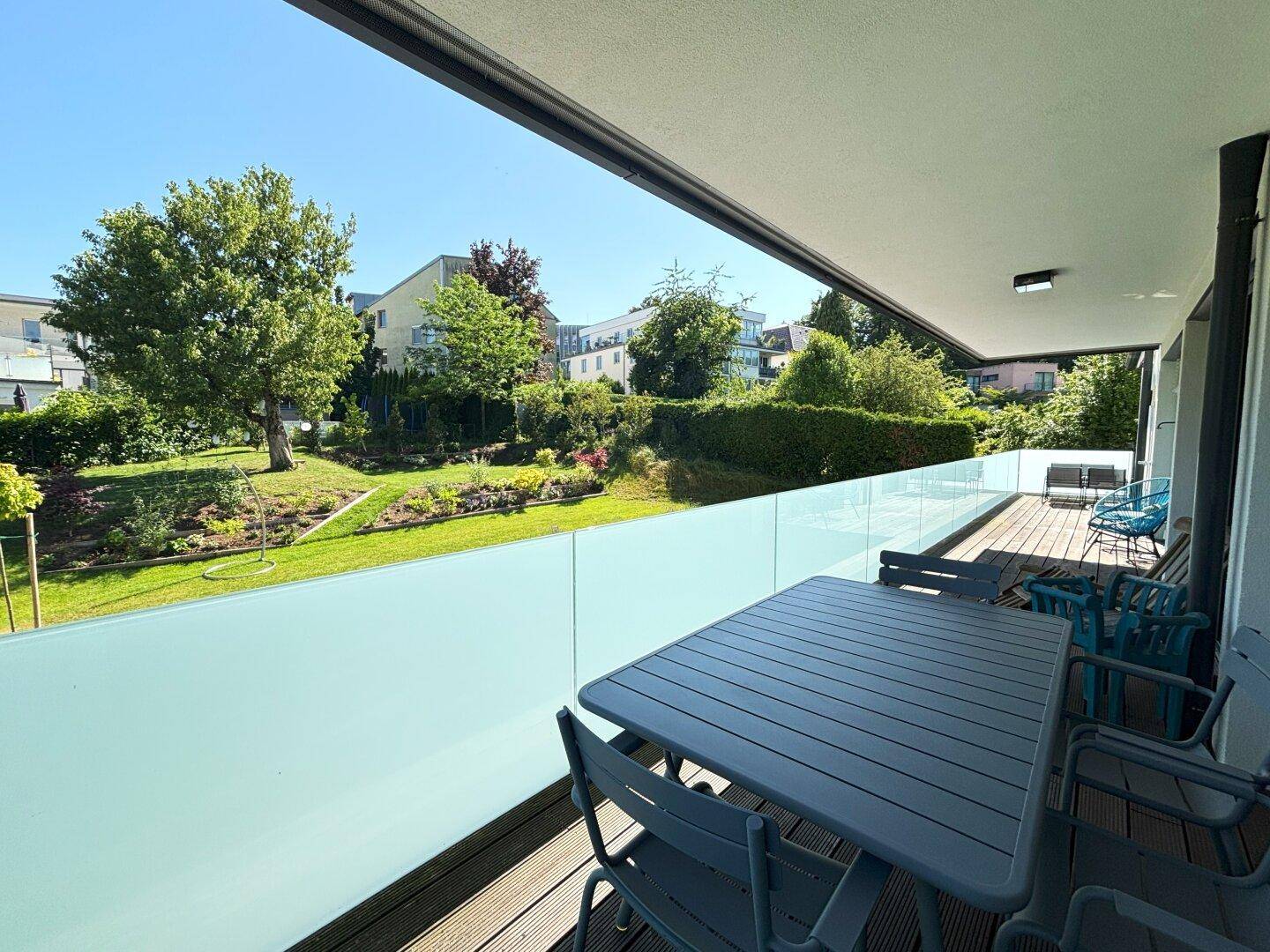 Geräumiger Balkon mit Holzboden, Glasbrüstung und Blick ins Grüne.
