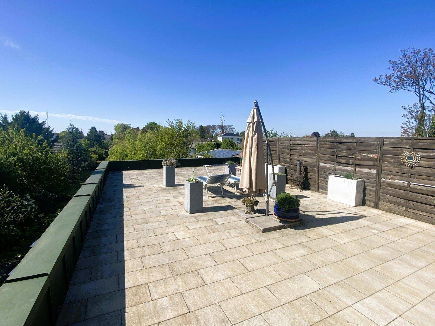 Weitläufige Dachterrasse mit Fliesenboden, Gartenmöbeln und weitem Blick in die Umgebung.