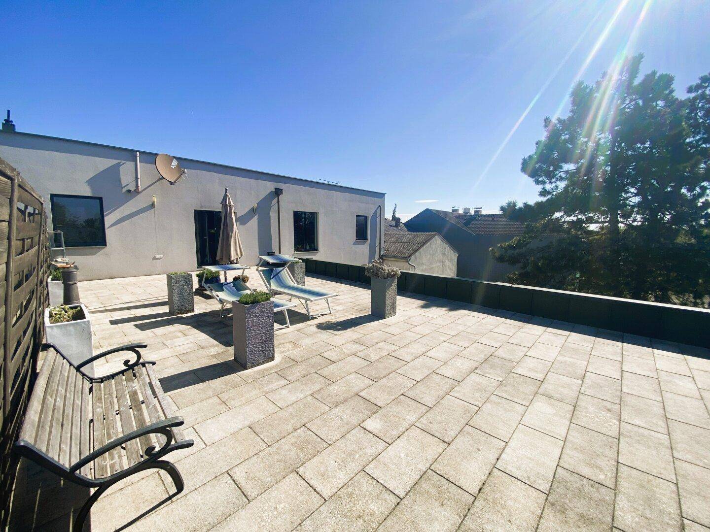 Sonnige Dachterrasse mit Liegestühlen, Bank und Blick auf die umliegenden Gebäude.