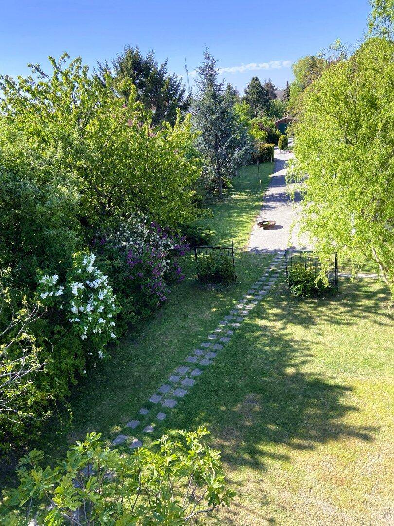 Langer Gartenweg mit Trittsteinen, umgeben von Bäumen und blühenden Sträuchern.