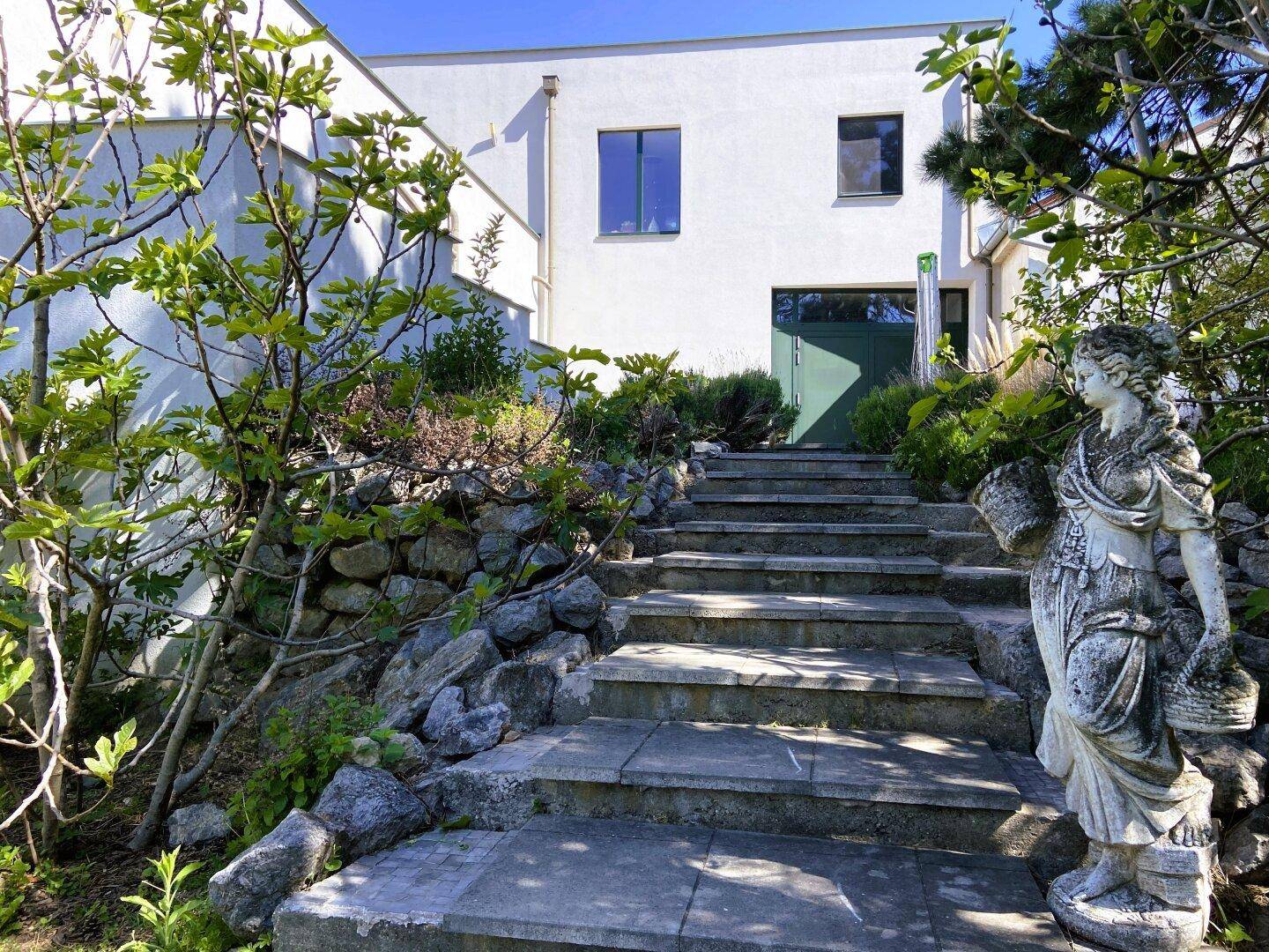 Eingangsbereich des Hauses mit Steintreppe, umgeben von Felsen und grüner Bepflanzung.