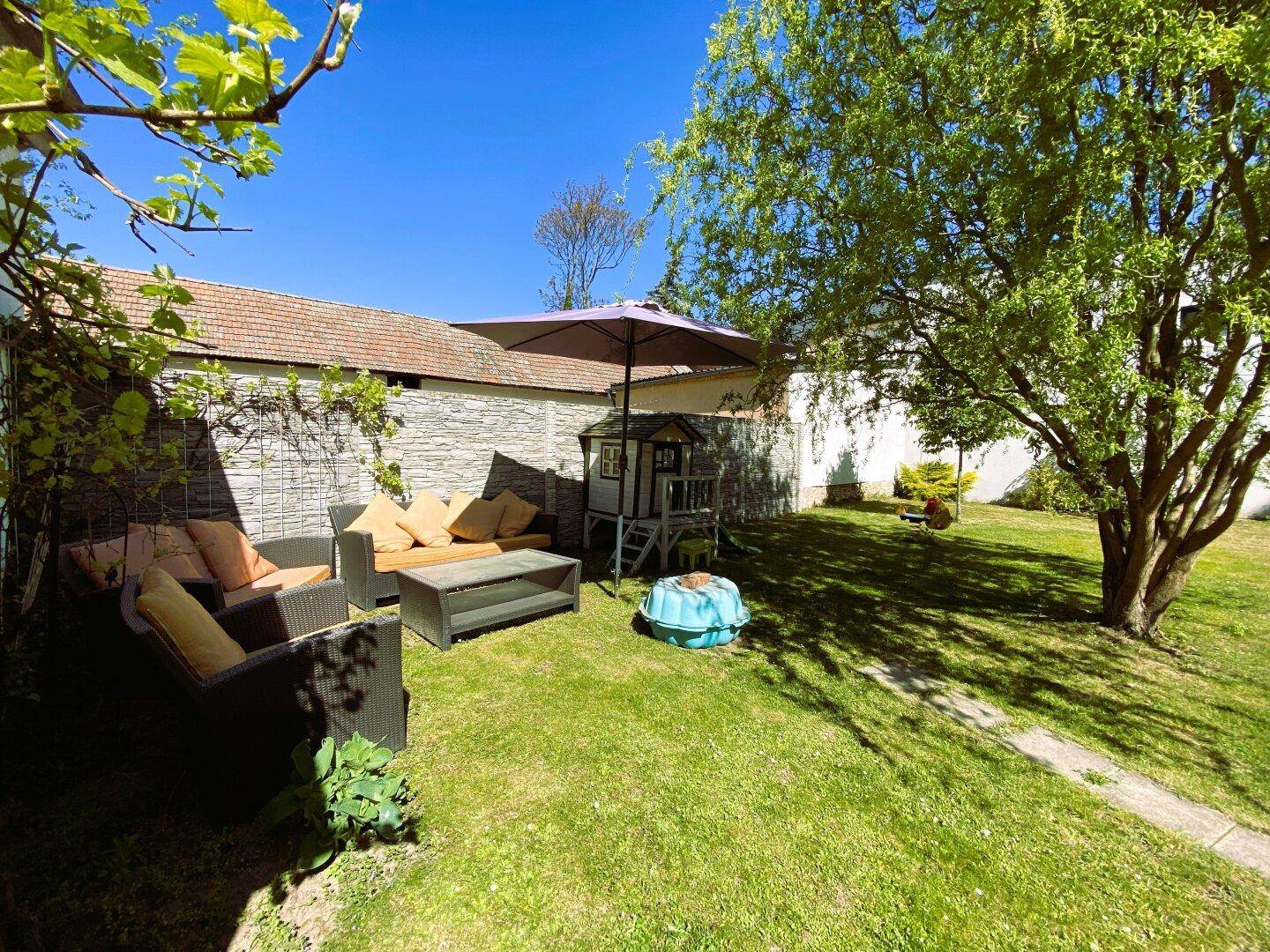 Gemütlicher Gartenbereich mit Lounge-Möbeln, Sonnenschirm und Spielzeug für Kinder.
