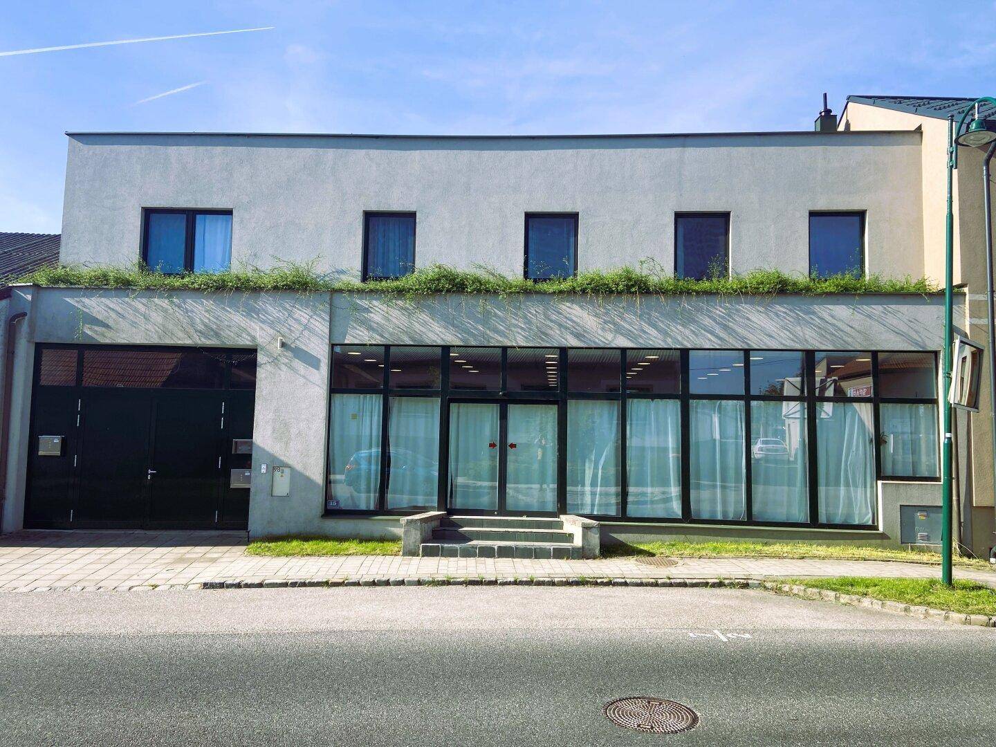 Moderne Geschäftsfassade mit großen Schaufenstern und darüberliegenden Wohnfenstern.