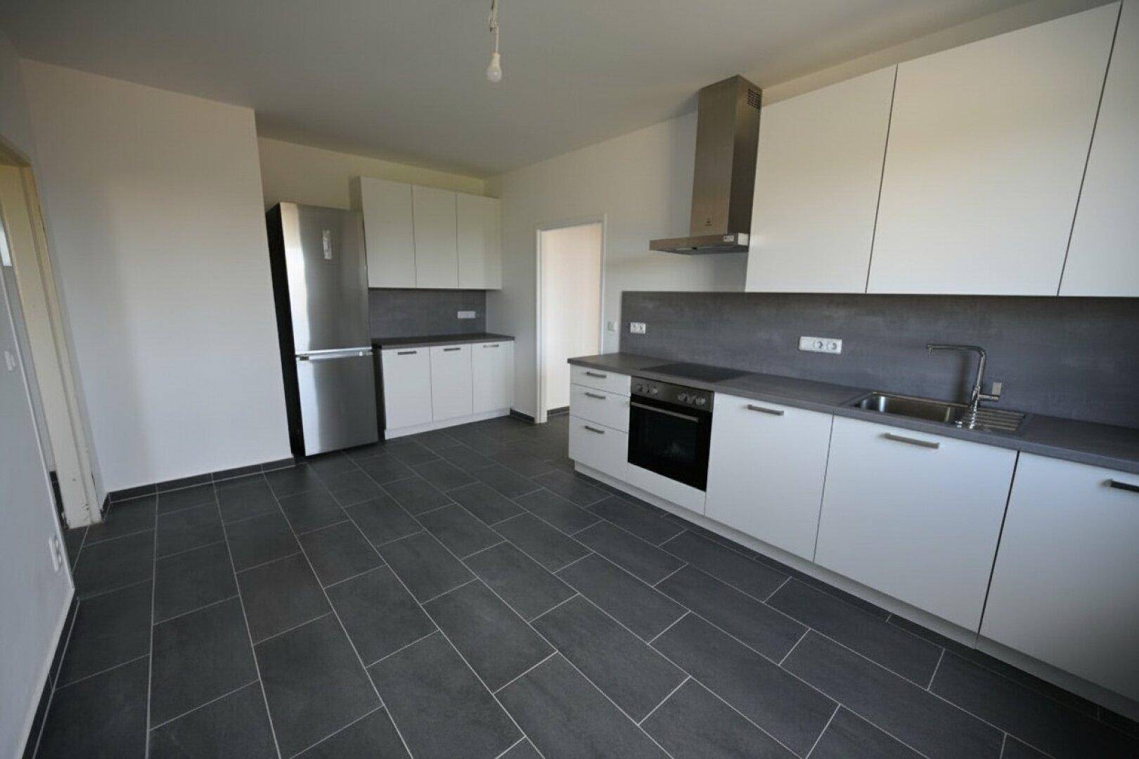 Moderne Einbauküche mit weißen Fronten, dunkler Arbeitsplatte, integriertem Kühlschrank und Fliesenboden.