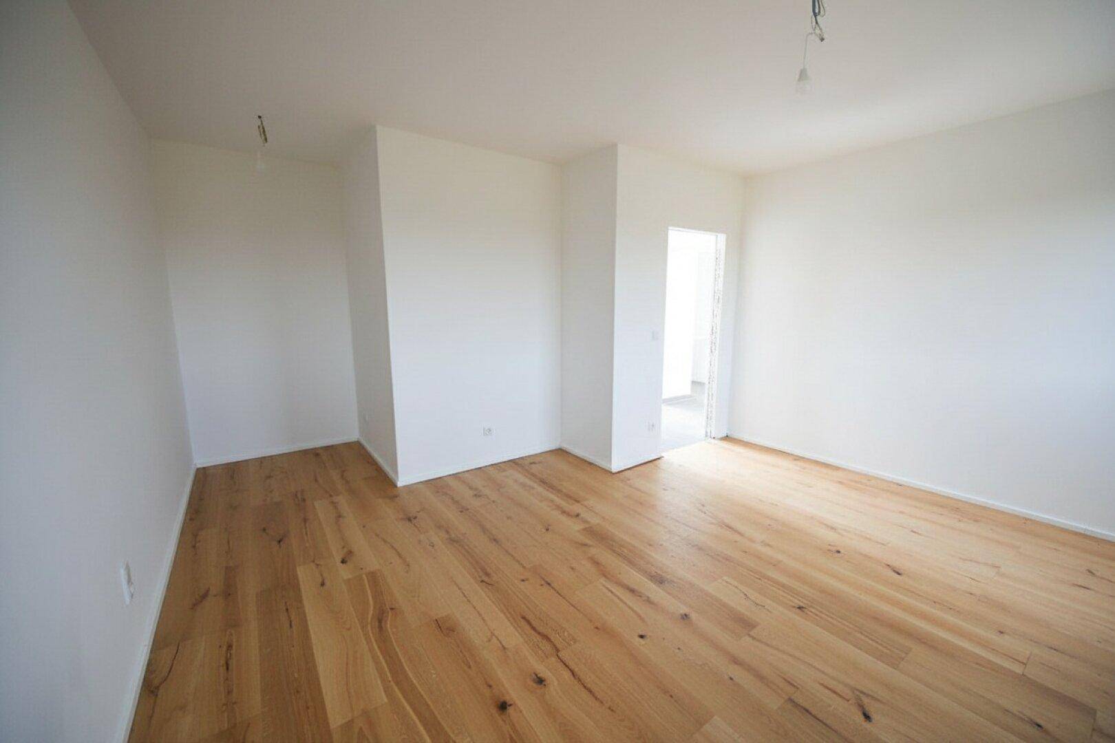 Leeres Zimmer mit warmem Holzboden und weiß gestrichenen Wänden, bereit zur individuellen Gestaltung.
