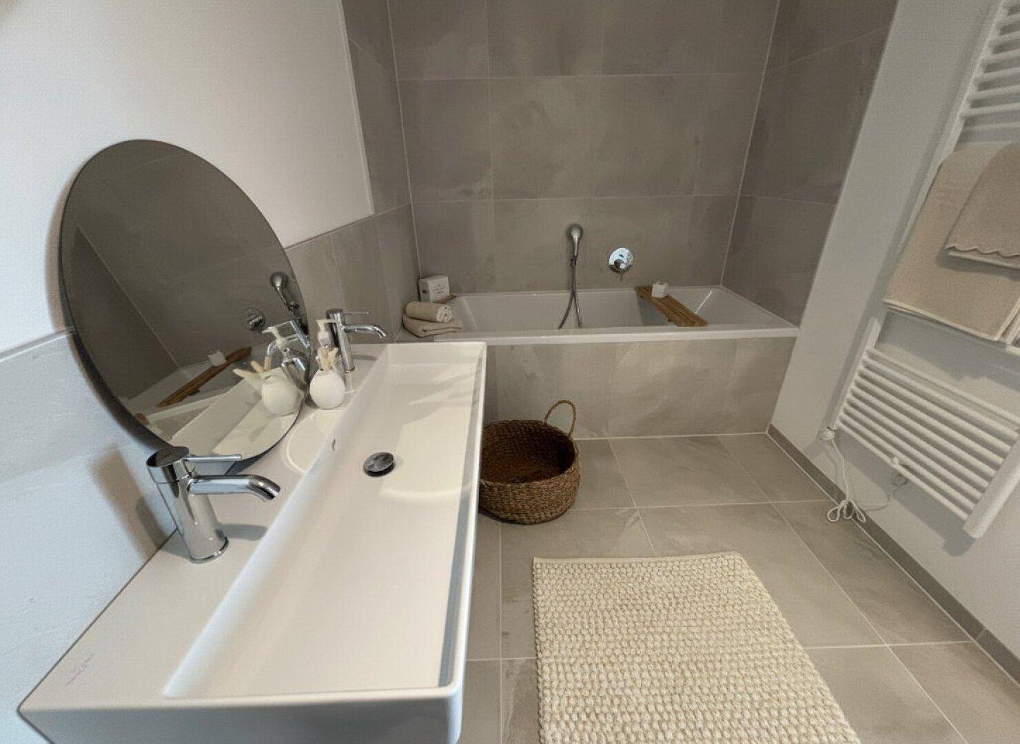 Detailansicht des modernen Badezimmers mit Doppelwaschbecken, Spiegel und Badewanne.