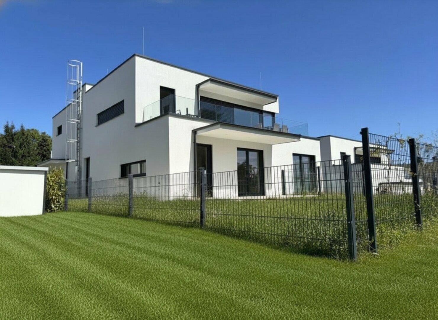 Moderne weiße Architektur mit klaren Linien, Balkonen und gepflegtem Rasenbereich.