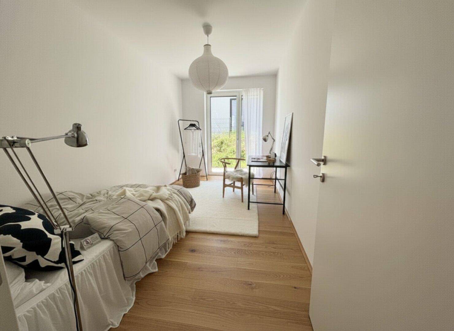 Helles Schlafzimmer mit Holzboden, minimalistischer Einrichtung und Zugang zu einem Außenbereich.