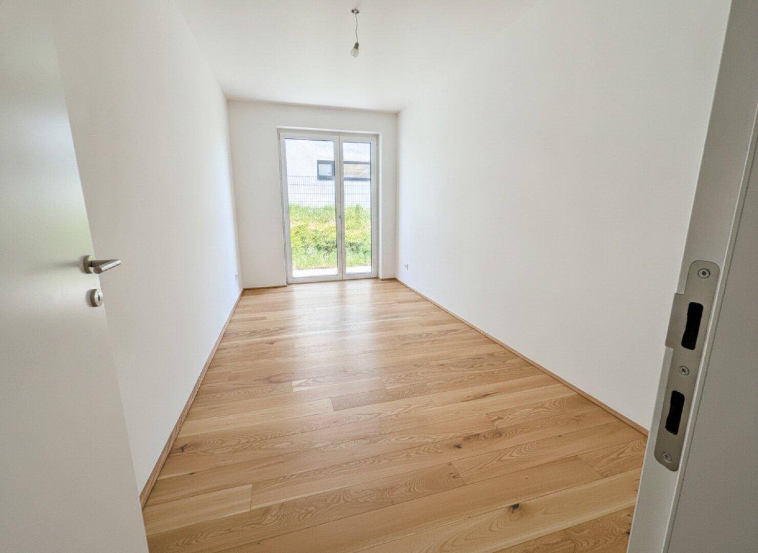 Helles Zimmer mit Eichenparkett und Zugang nach draußen, ideal als Schlaf- oder Arbeitszimmer.