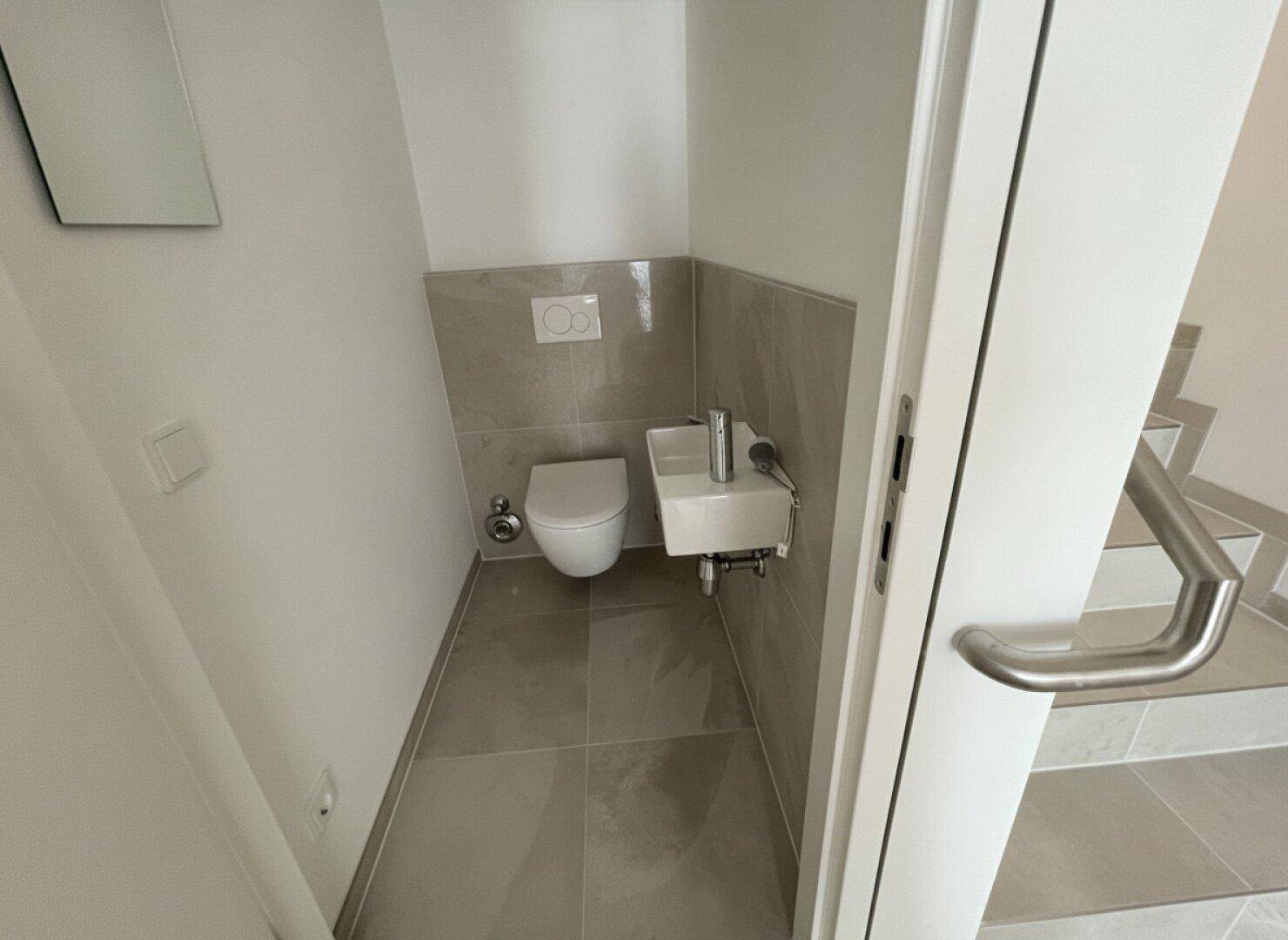 Praktisches Gäste-WC mit modernen Fliesen, wandhängender Toilette und kleinem Waschbecken.