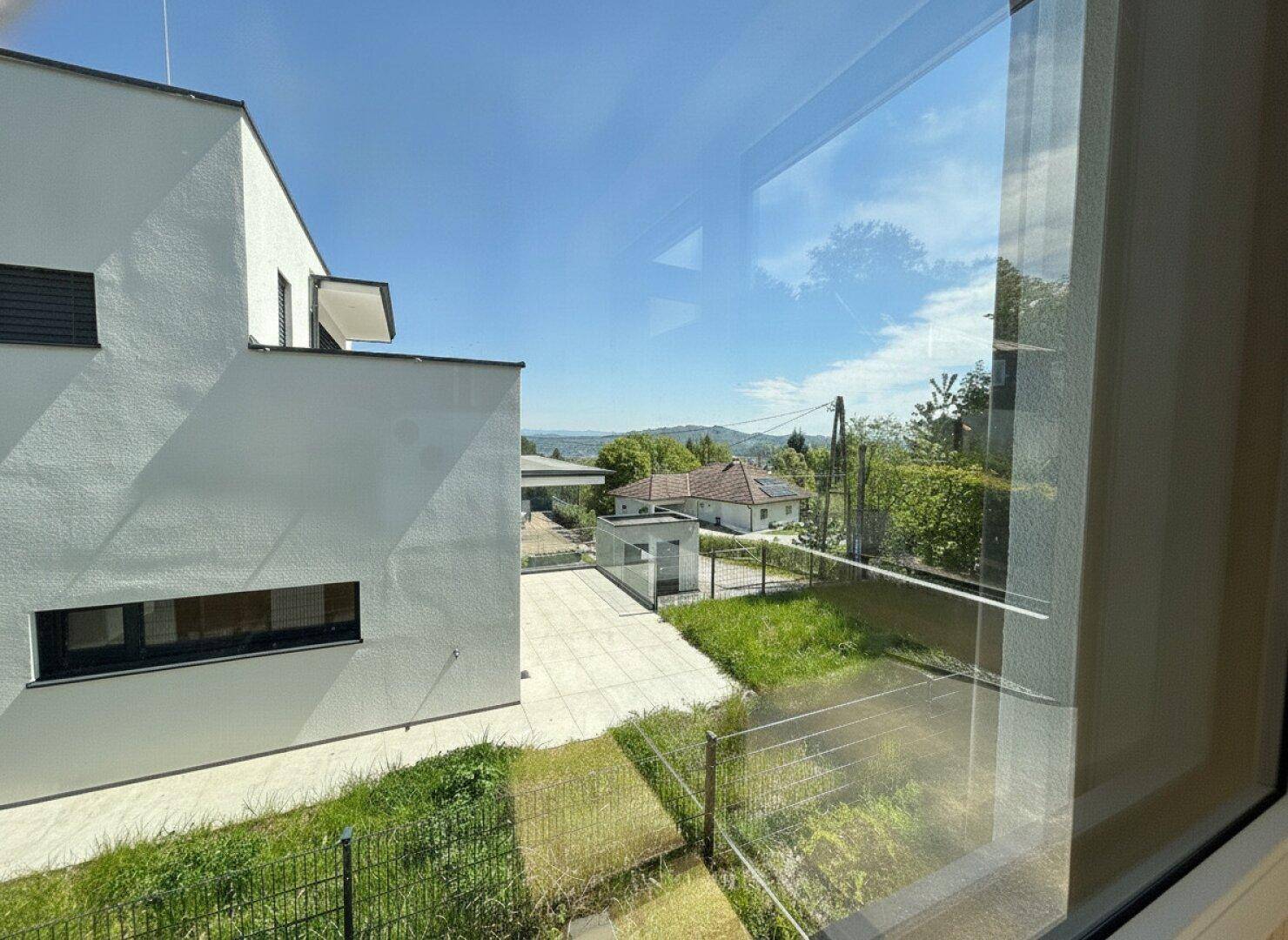 Blick aus dem Fenster auf das moderne Gebäude und die grüne Umgebung mit Fernsicht.