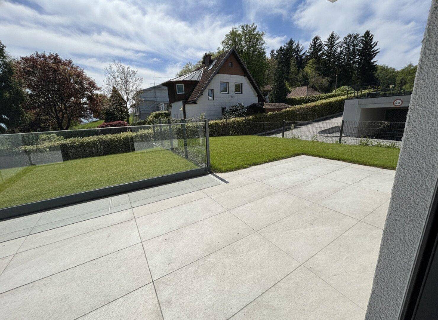 Sonniger Terrassenbereich mit Fliesen und Rasenfläche, bietet einen Blick auf die umliegende Bebauung.