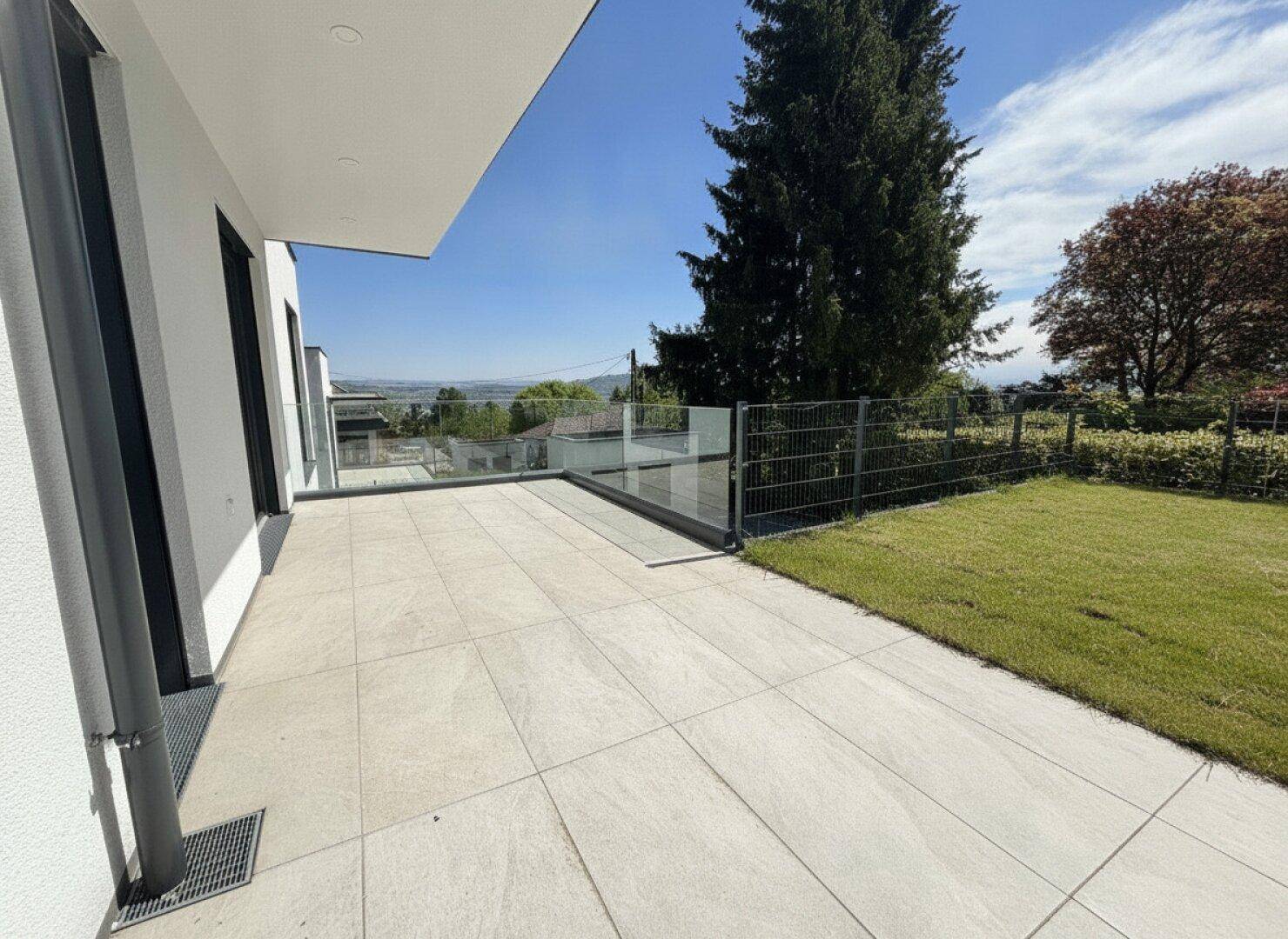 Geräumige Terrasse mit Glasgeländer und weitem Blick ins Grüne, umgeben von Rasenflächen.