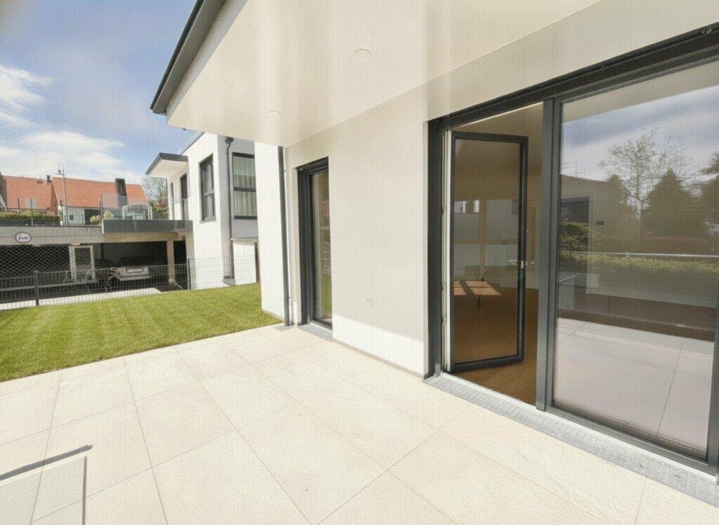 Moderne Terrasse mit hellen Fliesen und Zugang zum Garten, angrenzend an das Gebäude.