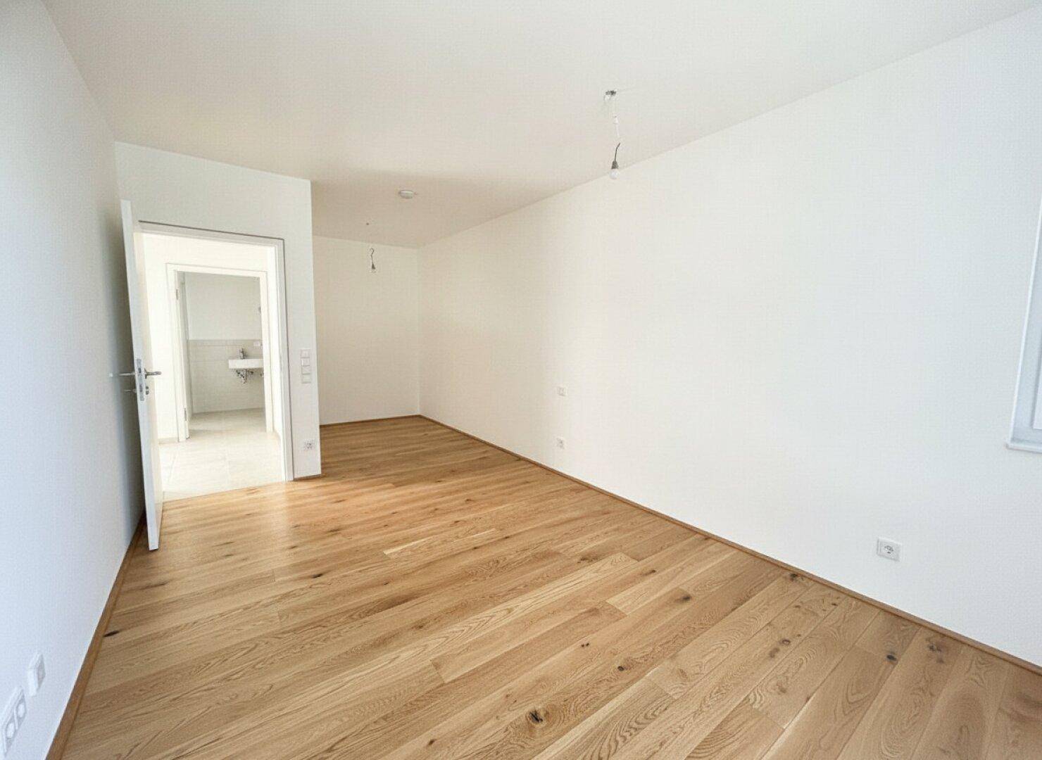Geräumiges Zimmer mit Eichenparkett und Blick in ein modernes Badezimmer, hell und einladend.