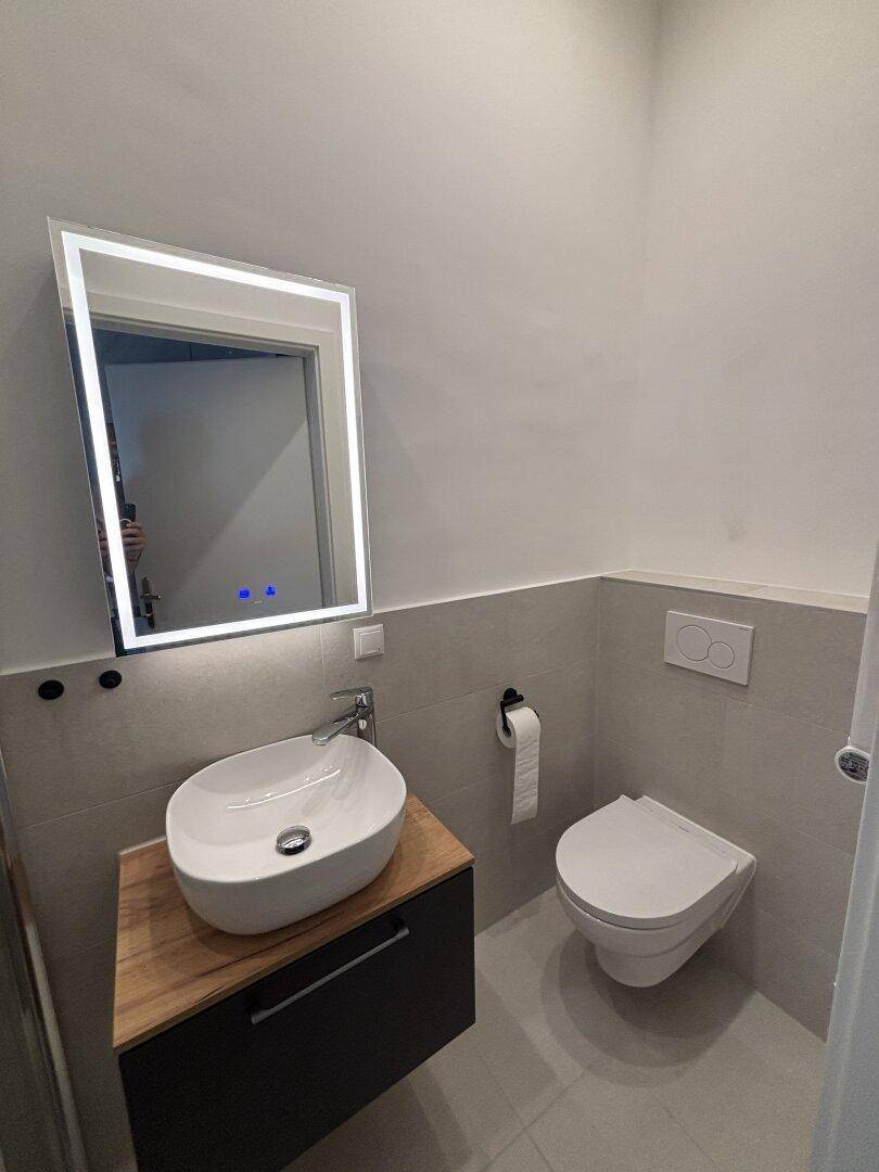 Modernes Gäste-WC mit stilvollem Aufsatzwaschbecken, beleuchtetem Spiegel und Wand-WC.