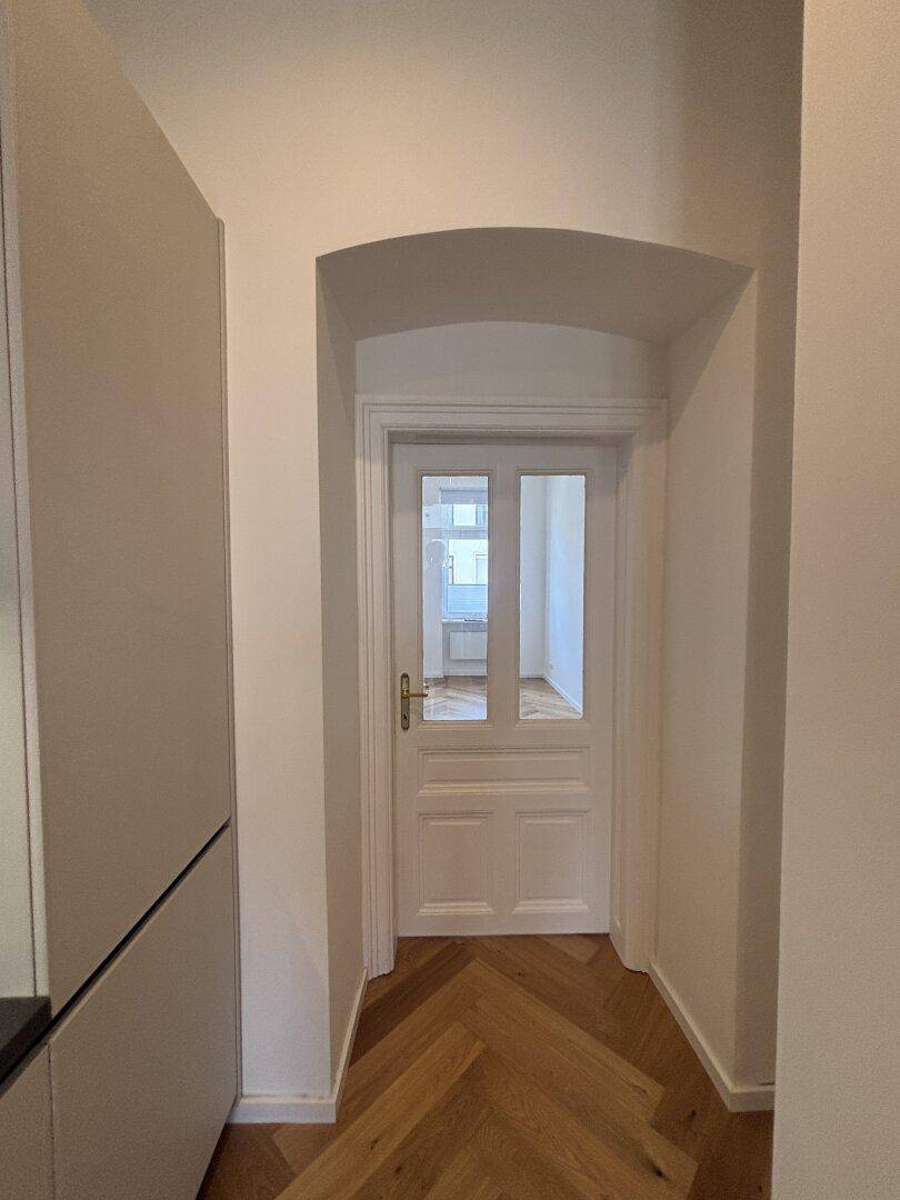 Heller Flur mit klassischem Fischgrätparkett und einer eleganten weißen Tür mit Glaseinsätzen.