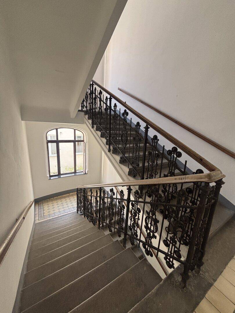 Historisches Treppenhaus mit kunstvollen schmiedeeisernen Geländern und einem Fenster auf halber Höhe.