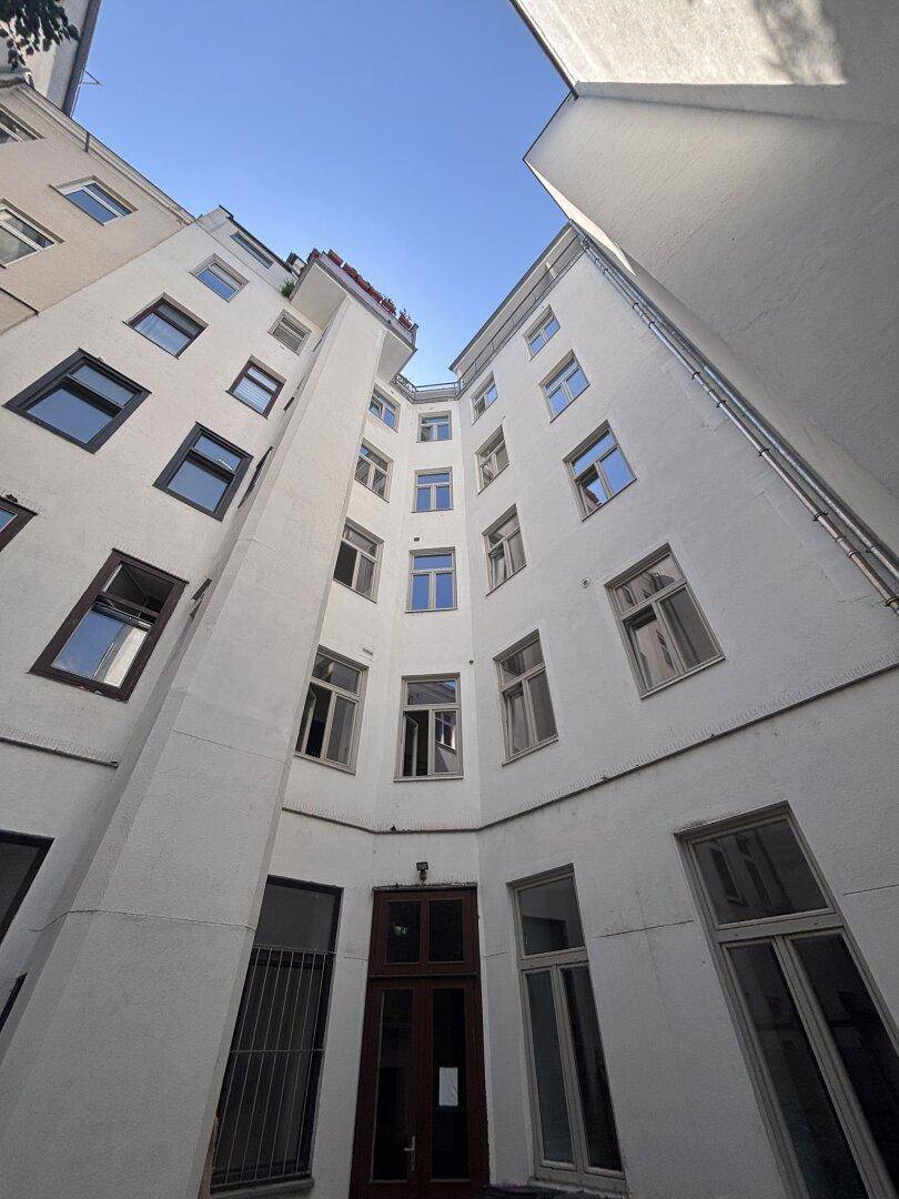 Blick nach oben in einen hellen Innenhof mit vielen Fenstern und einigen Balkonen.