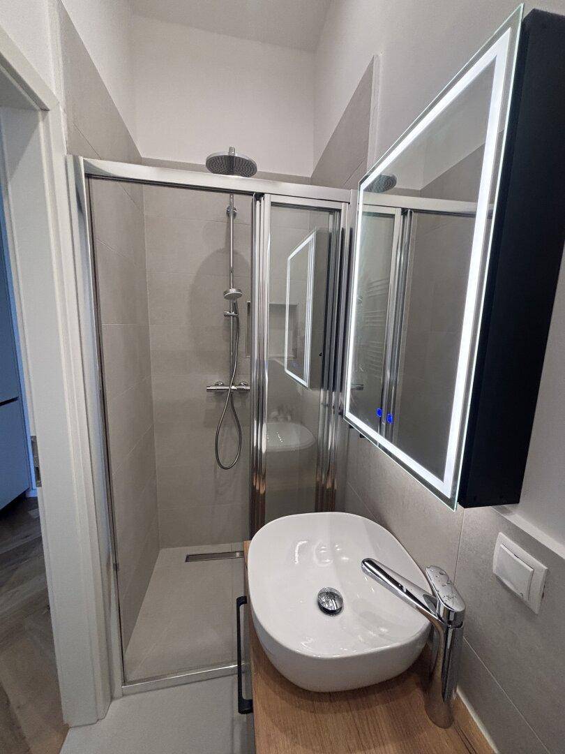 Elegantes Badezimmer mit begehbarer Dusche, modernem Waschbecken und beleuchtetem Spiegelschrank.