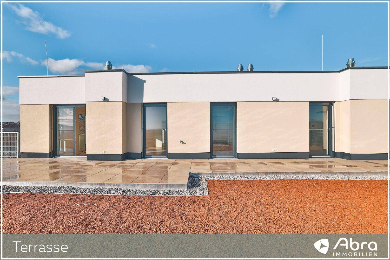 Moderne Gebäudefassade mit großer, gefliester Terrasse und Zugang zu den Innenräumen.