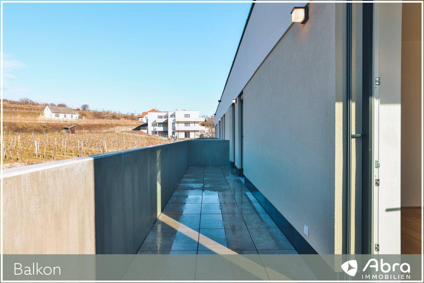 Langer, gefliester Balkon mit Betonbrüstung und Blick auf Weinberge und umliegende Häuser.