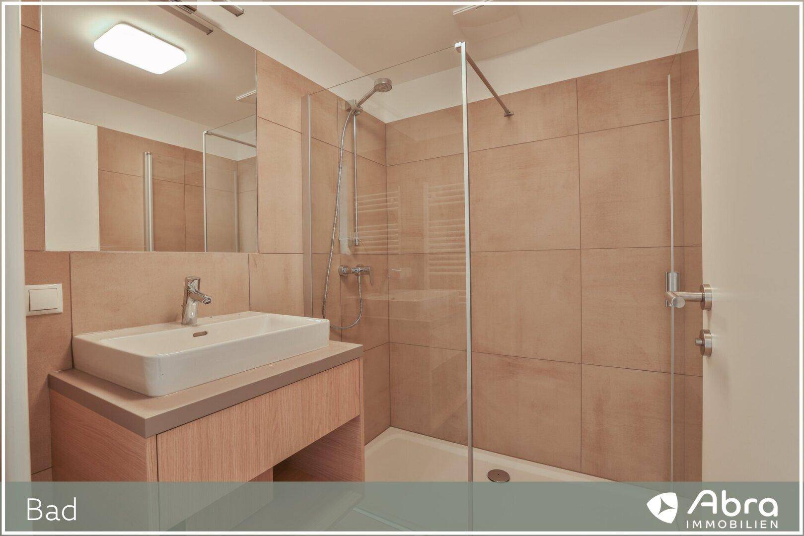 Modernes Badezimmer mit Waschtisch, Spiegel und einer geräumigen begehbaren Dusche mit Glasabtrennung.