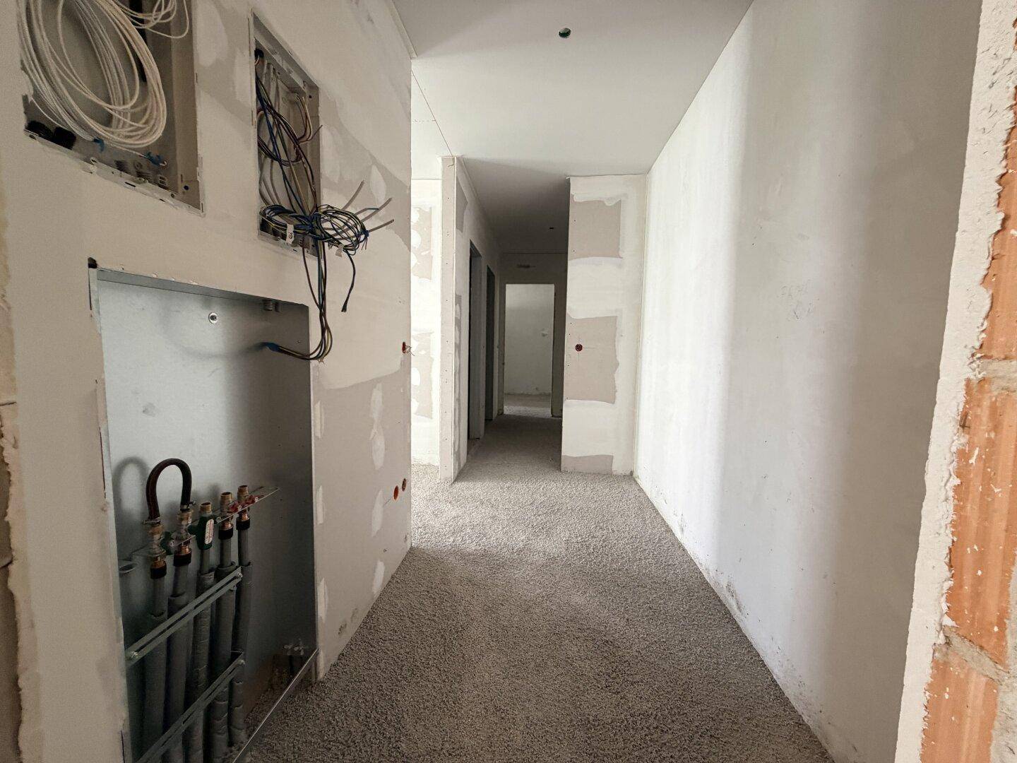 Unfertiger Flur im Rohbau mit sichtbaren Installationen und Estrichboden.