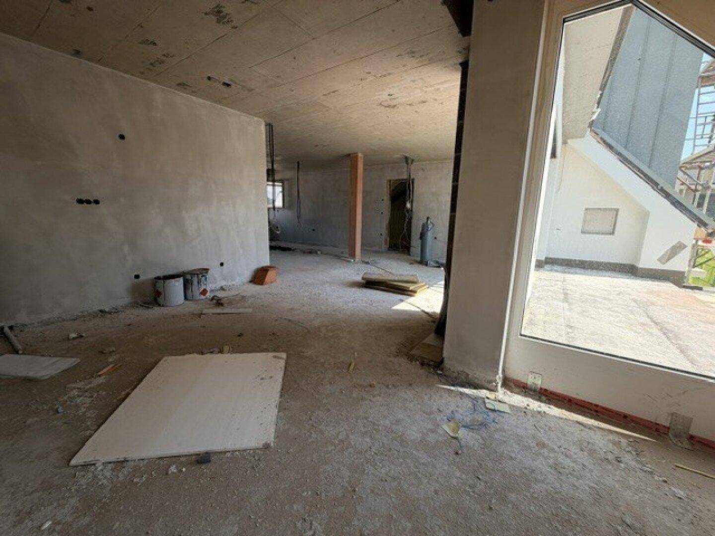 Rohbau eines hellen Raumes mit großen Fensterflächen, bereit für den weiteren Ausbau.