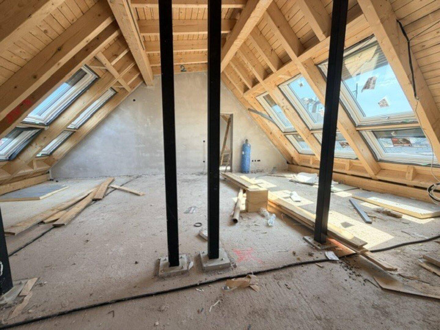 Dachgeschoss im Rohbau mit sichtbarer Holzkonstruktion, Stützbalken und zahlreichen Dachfenstern.