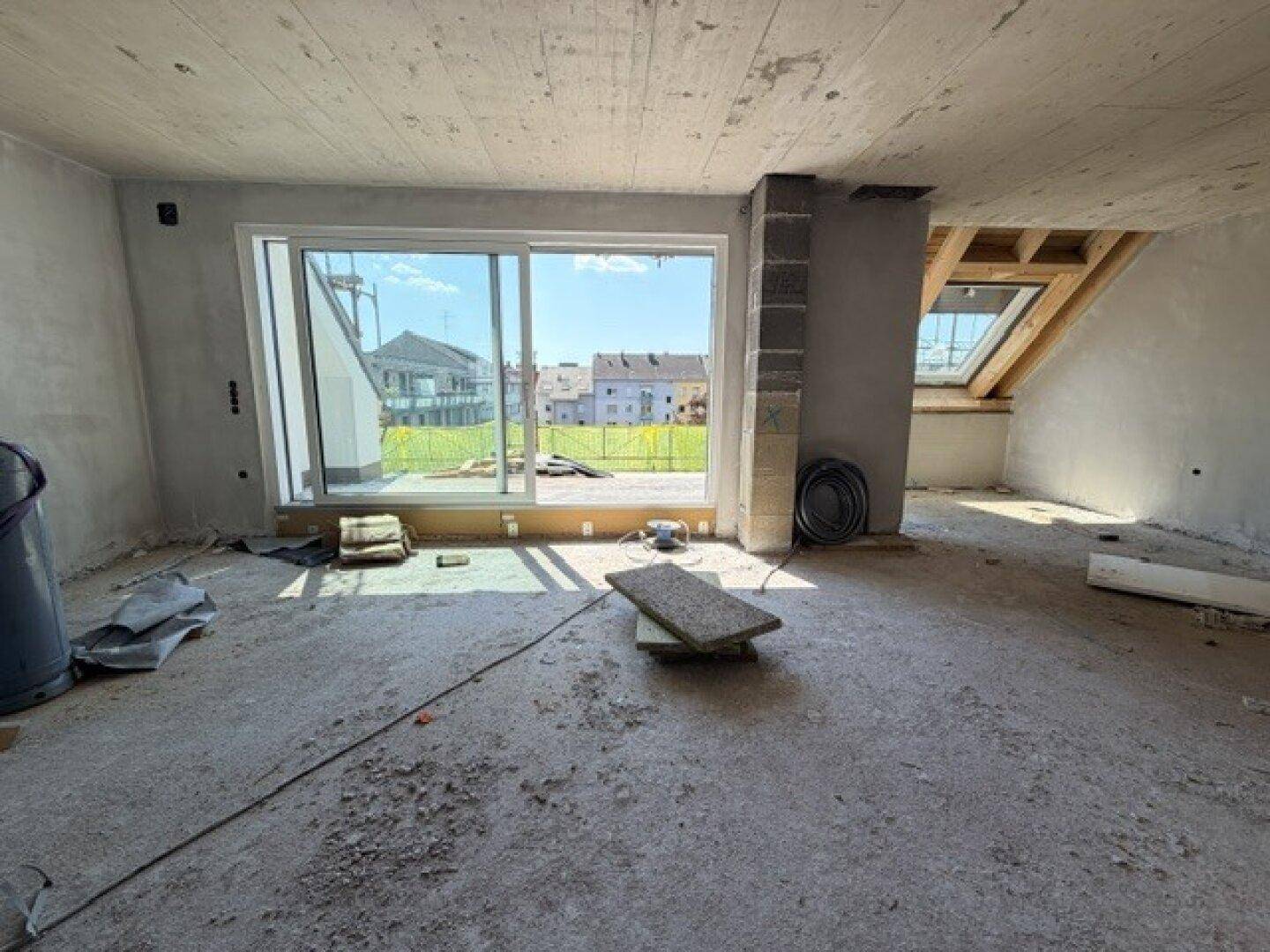 Unfertiger Innenraum im Dachgeschoss mit großen Fenstern und Blick ins Grüne während der Bauphase.